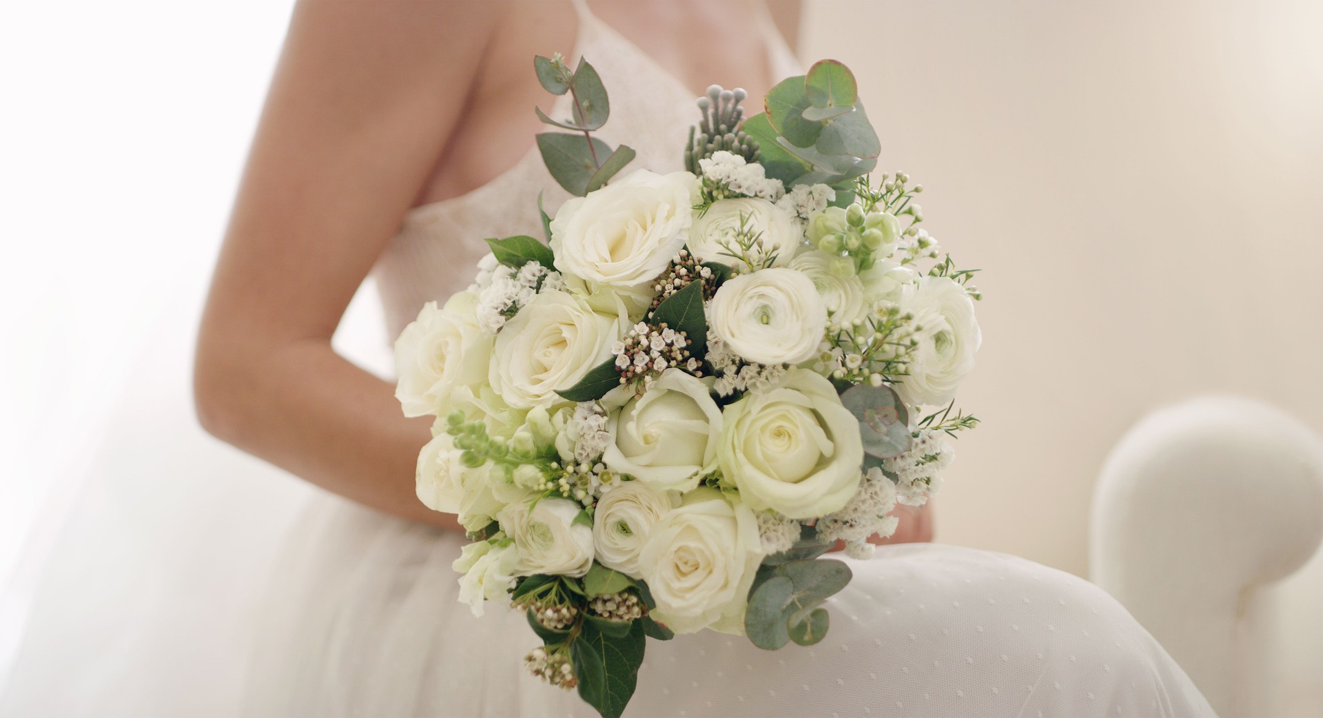 Bride holding bouquet of beautiful flowers on her wedding day, wearing an elegant white dress while sitting alone. Close up of a woman about to get married waiting with white roses and green leaves